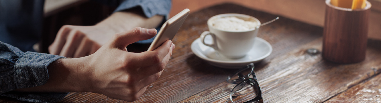 A man sitting at a wooden table with a cellphone in hand. 