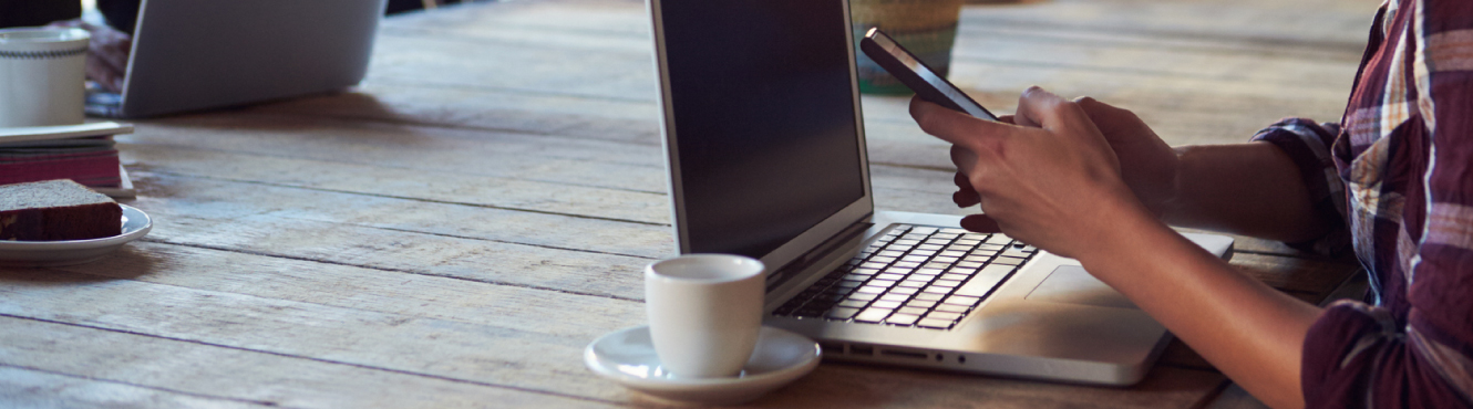 A person in front of a laptop using a mobile phone