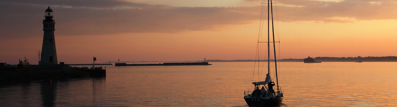 A view of a sunset over Lake Erie with a shadowed lighthouse and a sailboat.