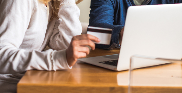 A close up of a couple using a debit card while on a laptop