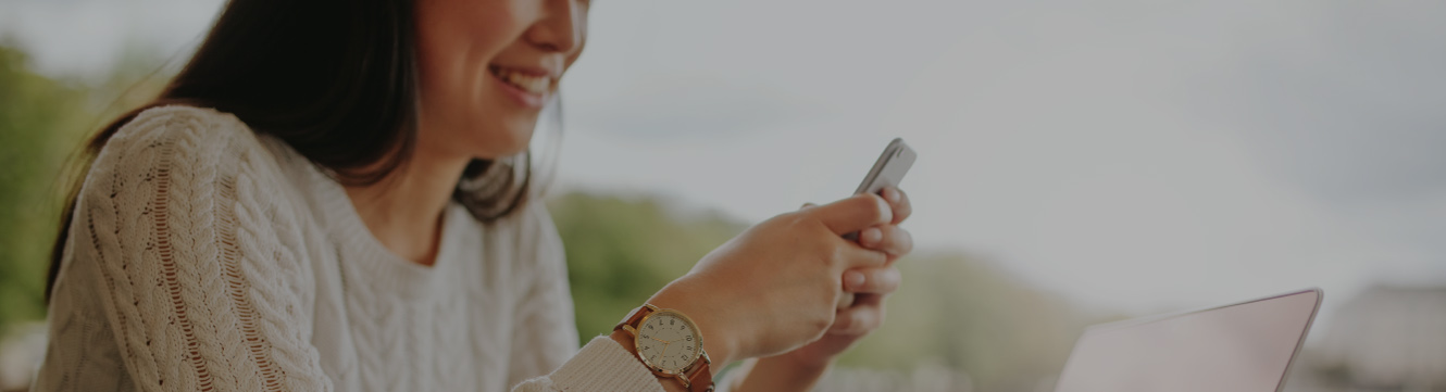 A woman smiles as she sits outside and looks at her cellphone.